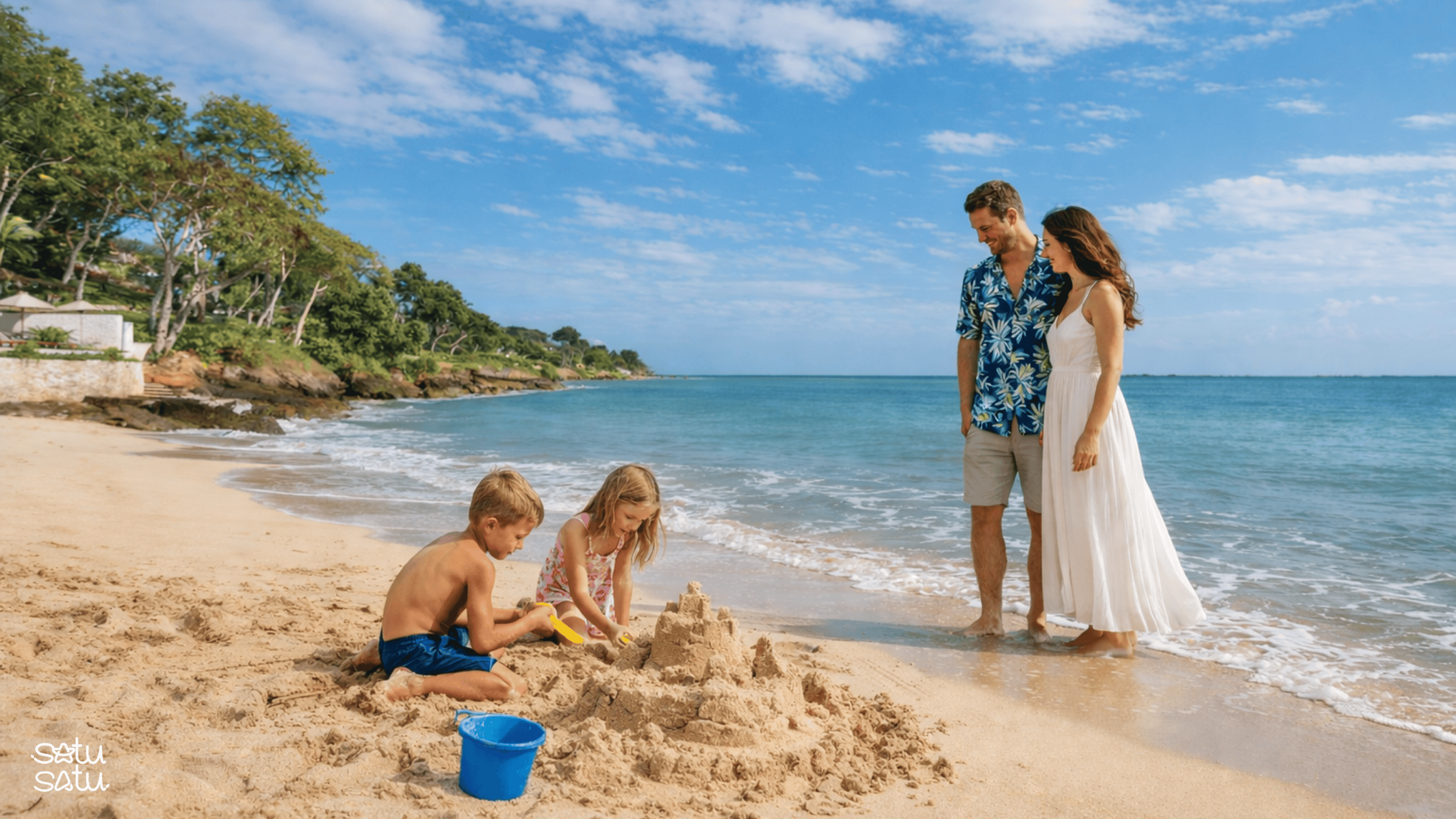 A family playing on the sand at Jimbaran Beach in Bali while children build a sandcastle by the sea.
