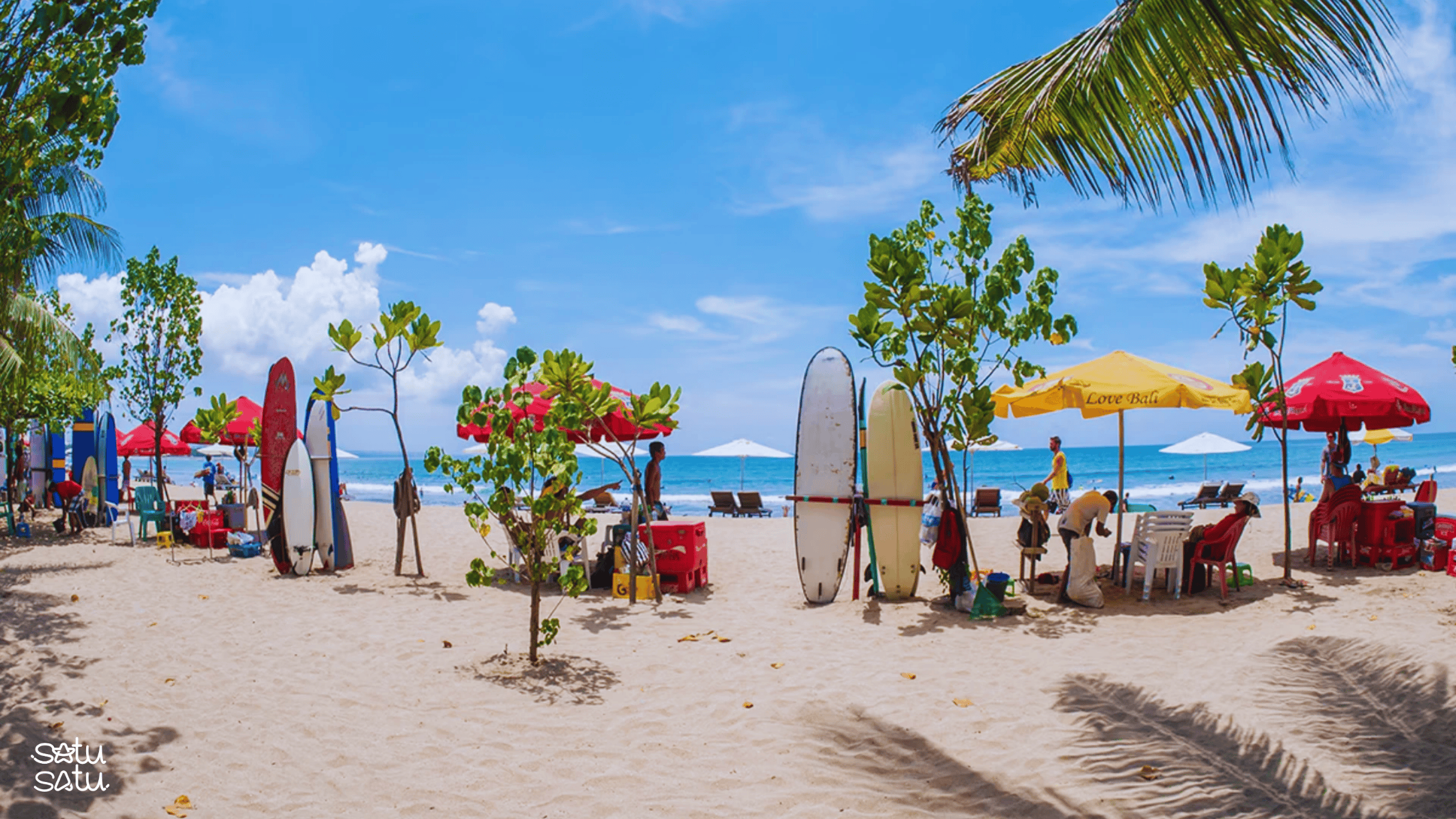 Kuta Beach in Bali with surfboards, beach umbrellas, and tourists enjoying the seaside atmosphere.