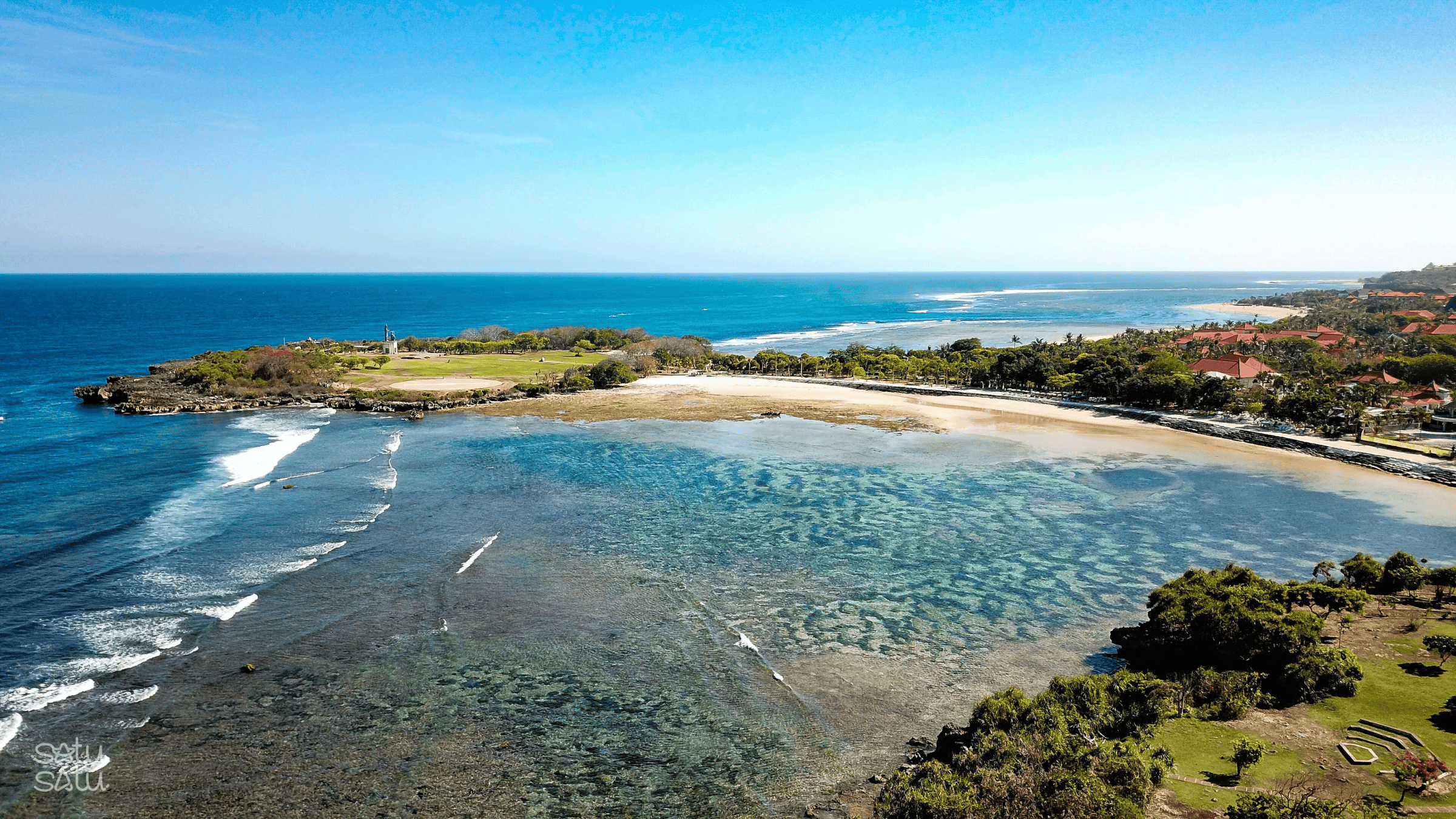 Aerial view of Nusa Dua Beach in Bali with clear turquoise water, coral reef patterns, and sandy shoreline along the coastline.