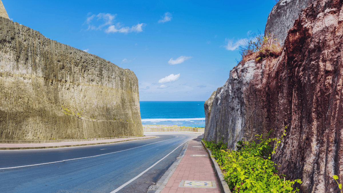Road between limestone cliffs leading to Pandawa Beach with ocean view in Bali.