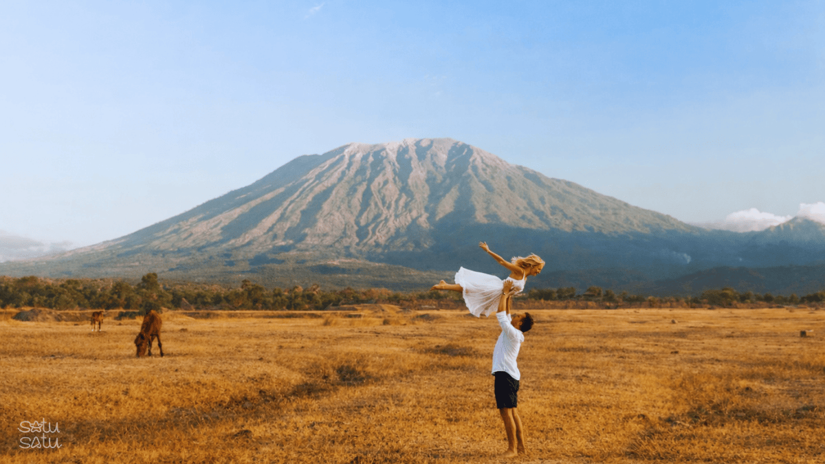 Couple enjoying Savana Tianyar in Karangasem Bali with Mount Agung in the background, surrounded by golden grassland landscape.