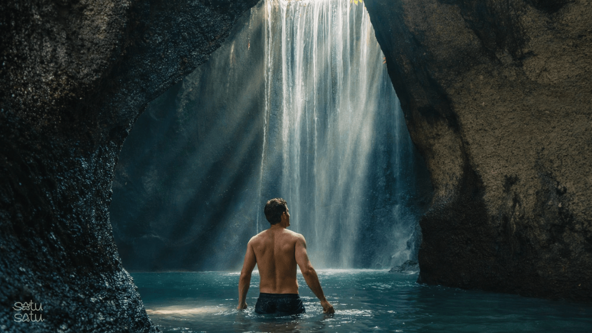 Traveler standing in the water beneath Tukad Cepung Waterfall, a hidden cave waterfall in Bali known for its dramatic sun rays.