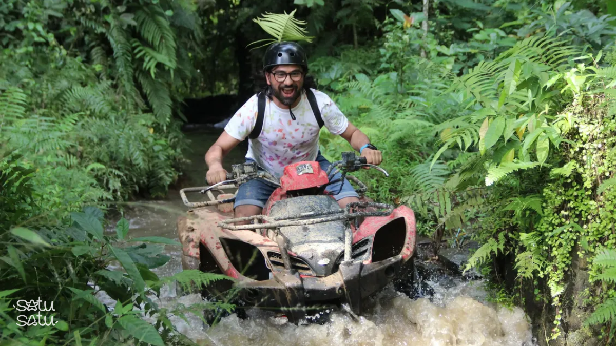 Man riding an ATV through a muddy jungle stream in Ubud Bali during an off-road adventure tour.