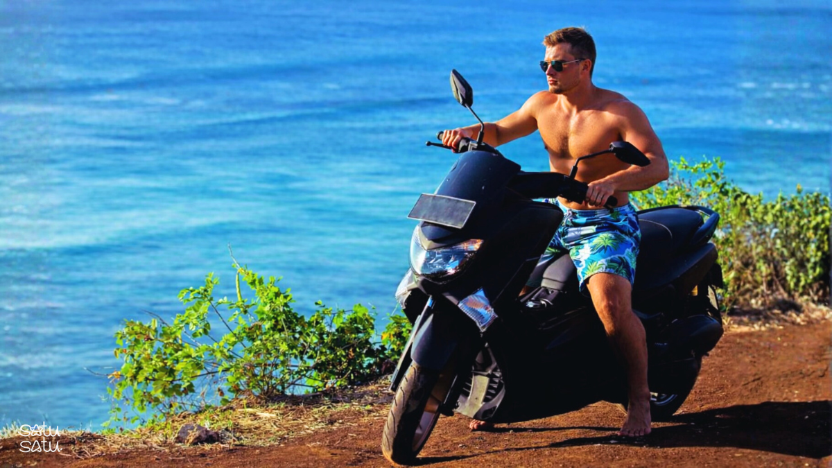 Traveler riding a scooter along a scenic coastal road in Bali with ocean views