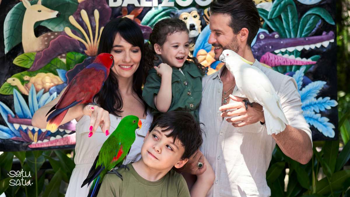 Family interacting with colorful tropical birds during an animal encounter at Bali Zoo.