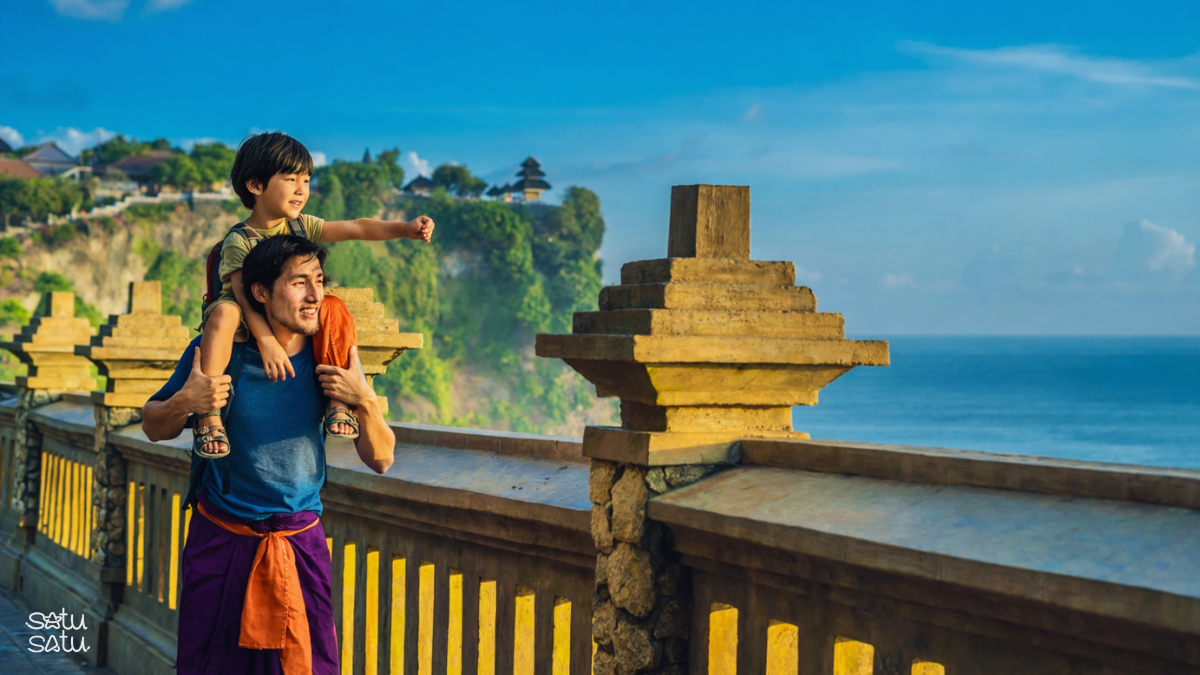 Father carrying his son while exploring the scenic cliffside area of Uluwatu Temple in Bali with ocean views in the background