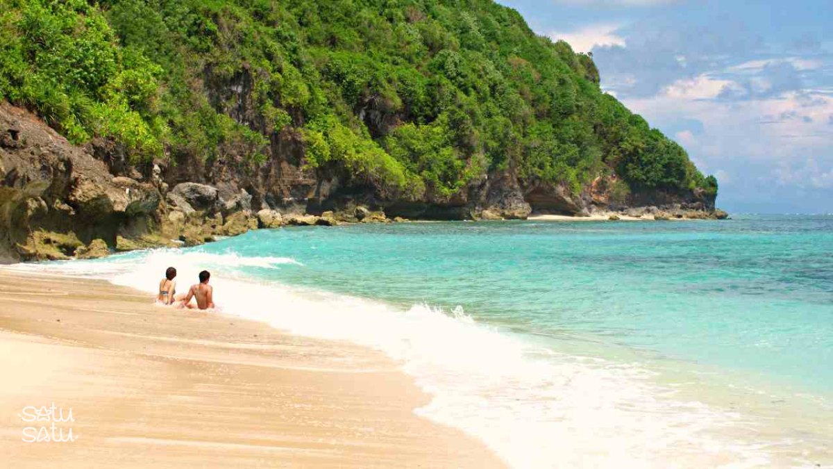 Travelers relaxing on the shoreline of Green Bowl Beach in Bali with turquoise water and limestone cliffs