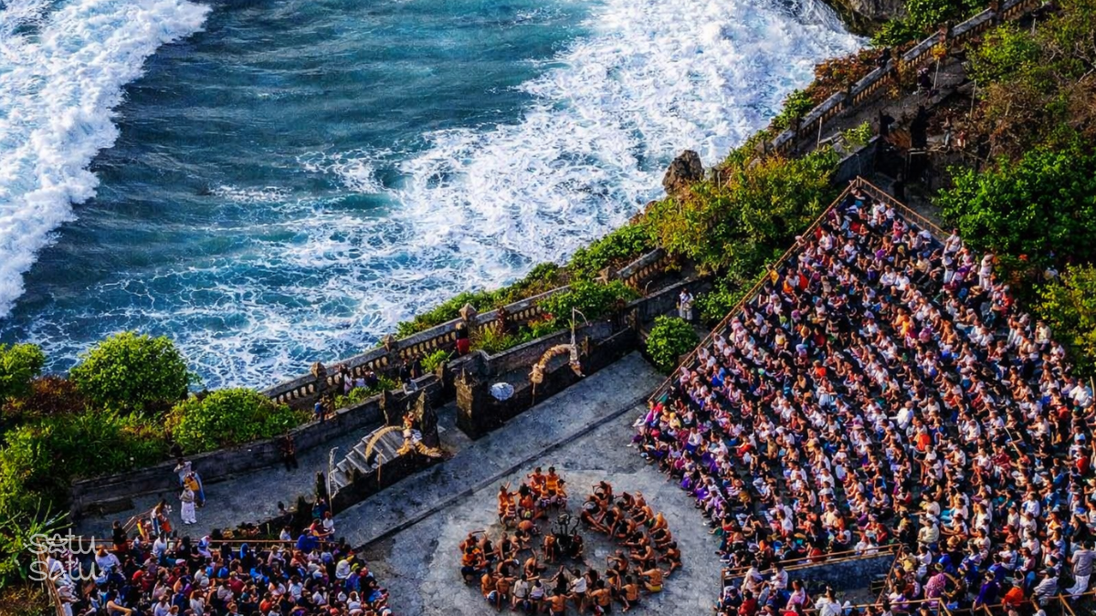 Aerial view of Kecak dance performance at Uluwatu Temple with ocean waves and large audience in Bali