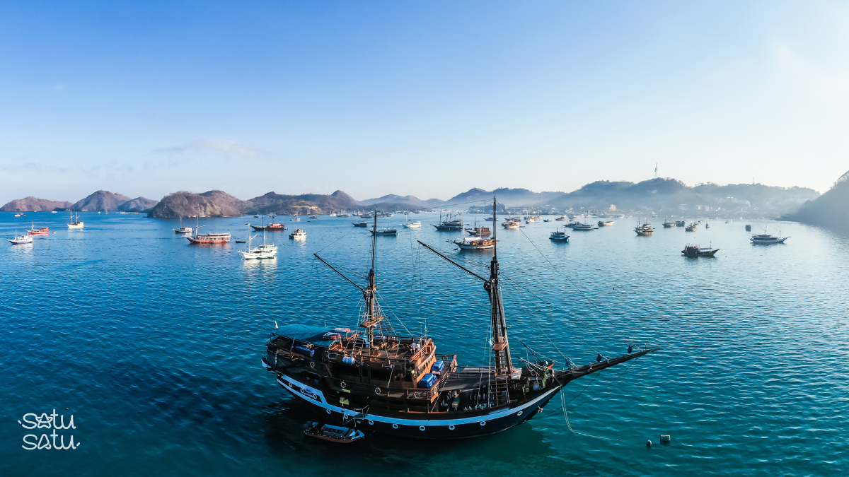 Traditional boats anchored in the calm waters of Labuan Bajo harbor with island views in Flores, Indonesia.
