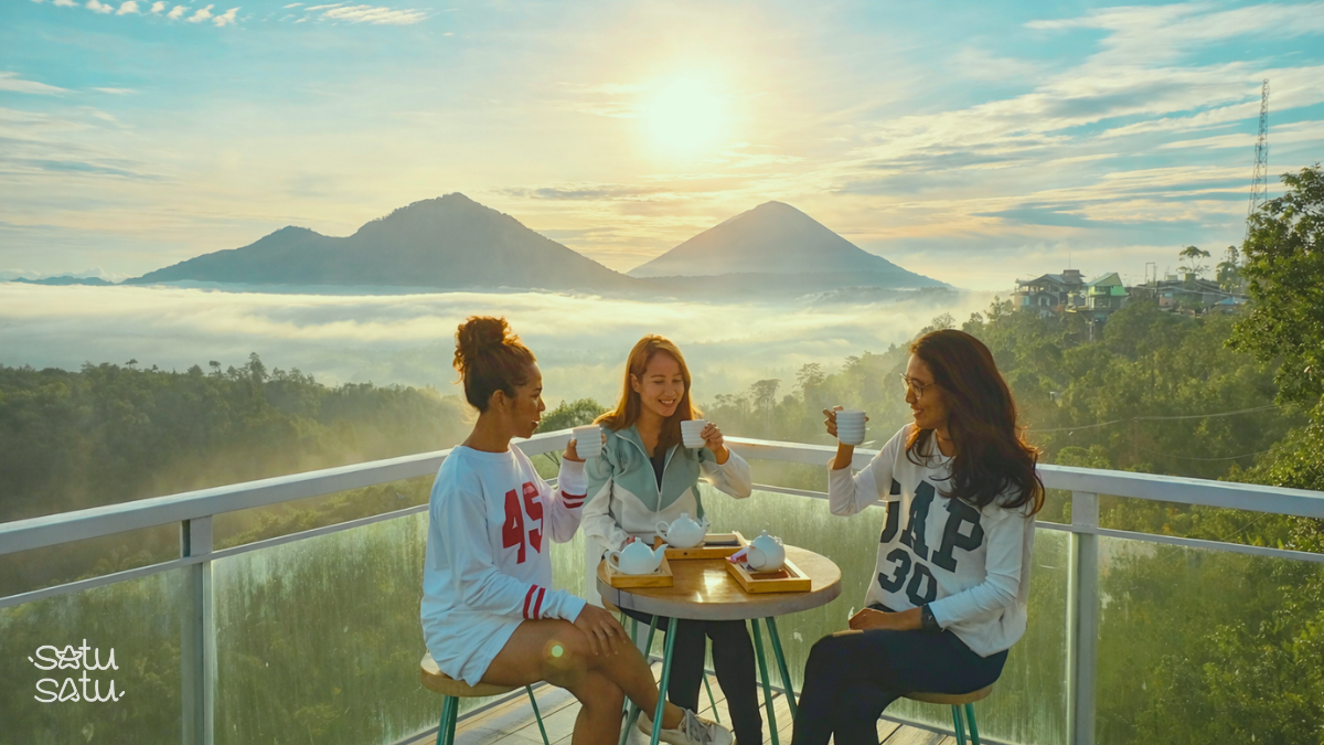 Travelers enjoying morning coffee with Mount Batur and misty valley views from a café in Kintamani, Bali.