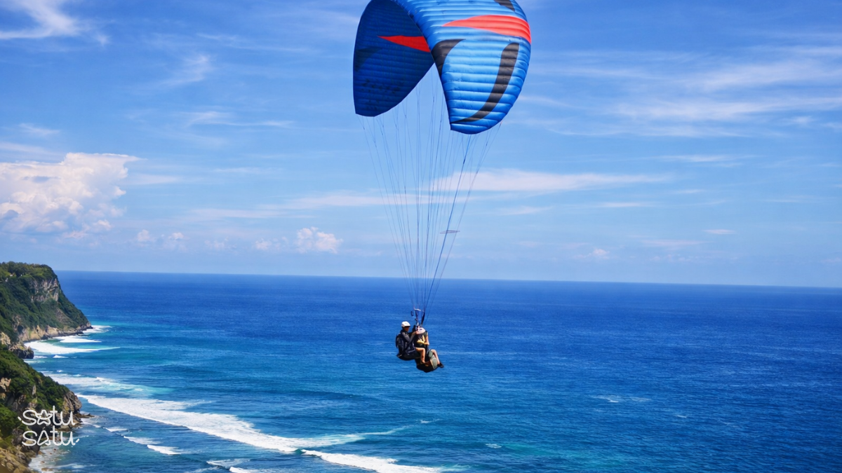 Paragliding over Timbis Beach in Bali with panoramic ocean views and dramatic coastal cliffs.