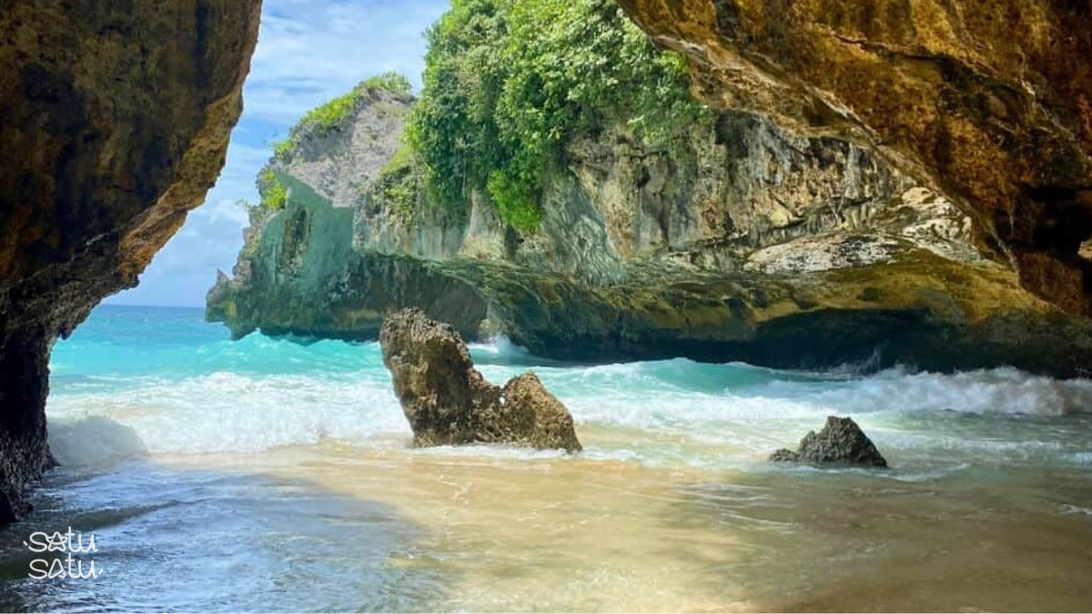 Ocean waves entering the rocky cave opening at Suluban Beach in Bali with limestone cliffs and turquoise water