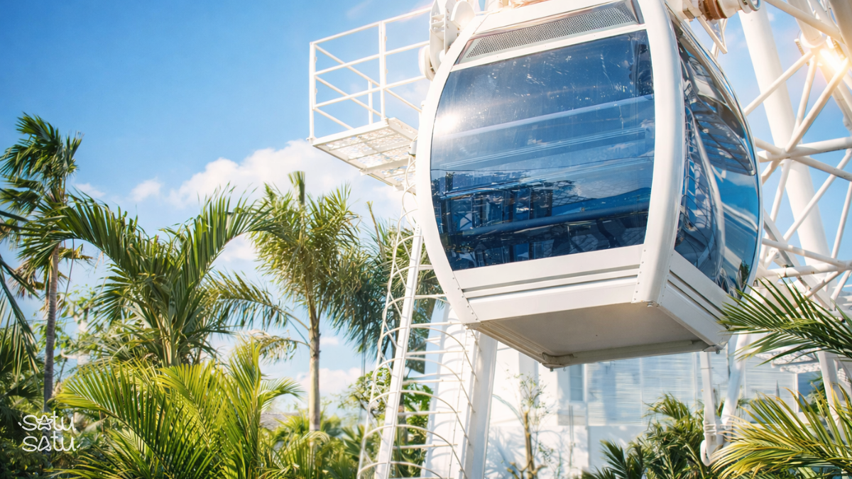 Close-up of a glass cabin on The Wheel Bali observation wheel in Canggu surrounded by tropical palm trees.